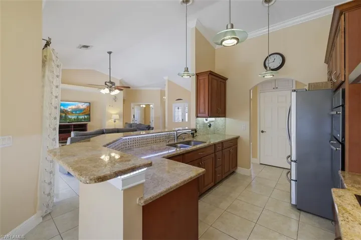 Kitchen featuring a peninsula, light stone counters, crown molding, light tile patterned floors, and wood finish cabinetry