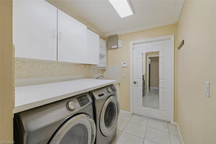 Laundry room with light tile patterned flooring, crown molding, cabinet space, and washing machine and clothes dryer