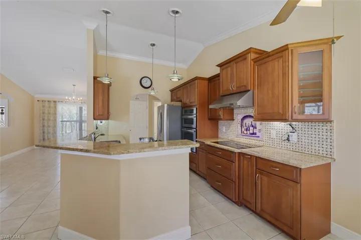 Kitchen featuring wood finish cabinets, decorative backsplash, ornamental molding, light stone counters, and glass fronted cabinets