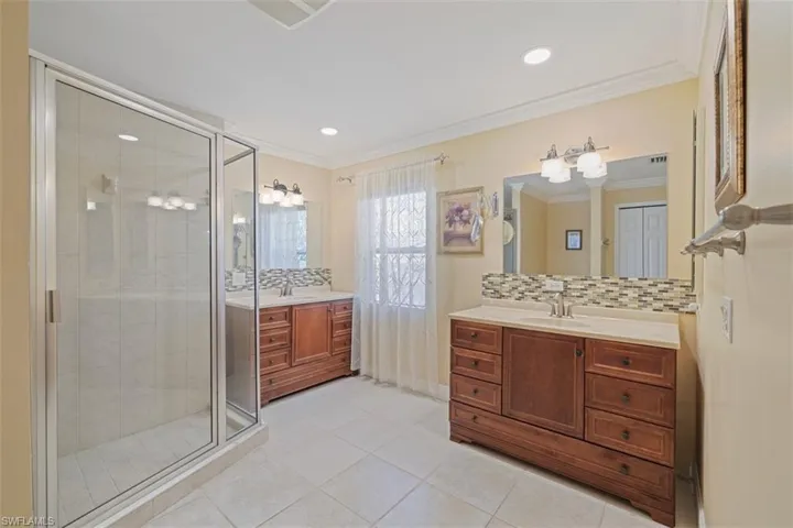Full bath featuring two vanities, backsplash, a shower stall, light tile patterned floors, and crown molding