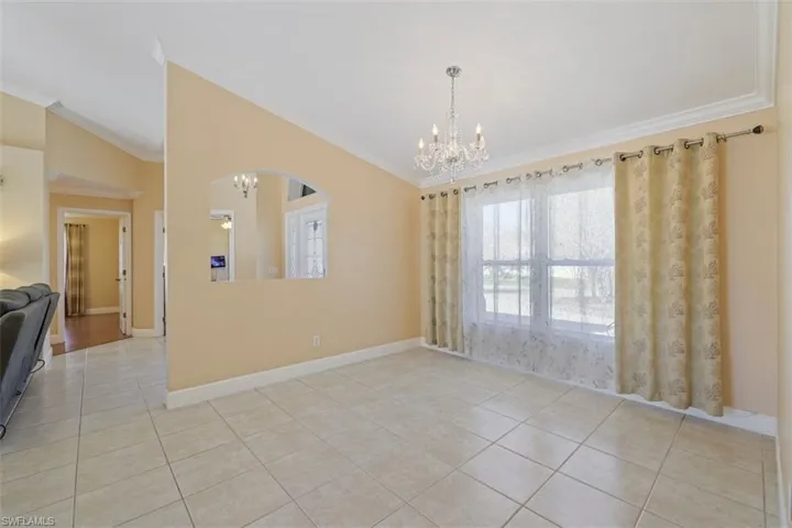 Empty room featuring suspended lighting, lofted ceiling, light tile patterned floors, and ornamental molding