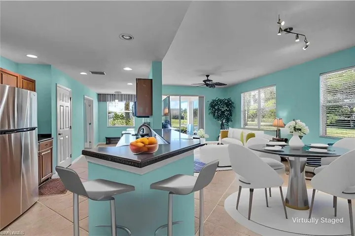 Kitchen featuring ceiling fan, light tile flooring, track lighting, a breakfast bar area, and stainless steel refrigerator