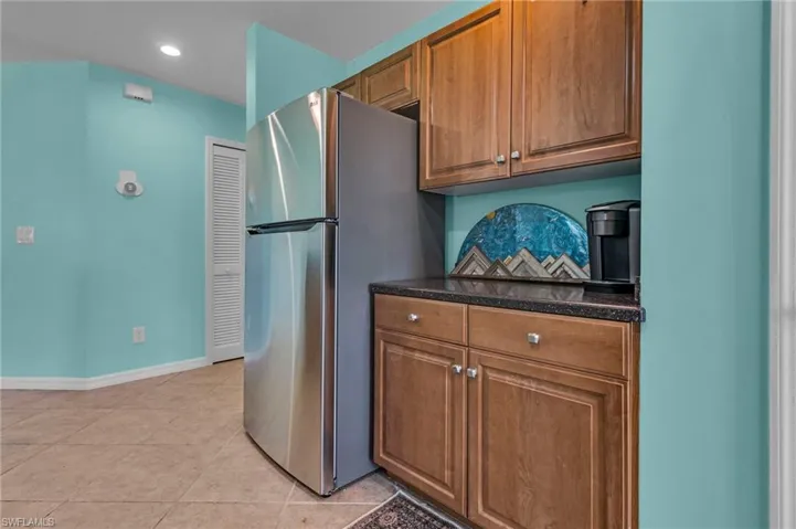 Kitchen with dark stone countertops, stainless steel refrigerator, and light tile flooring