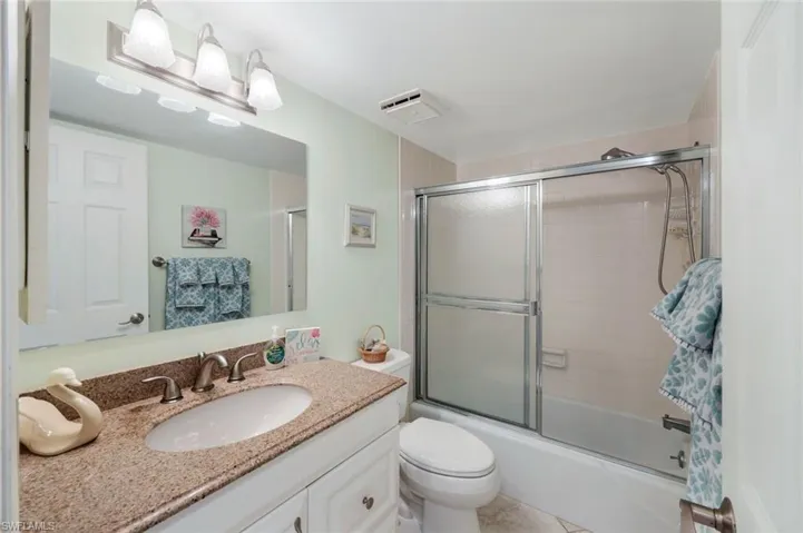 Full bathroom with vanity, bath / shower combo with glass door, toilet, and tile patterned floors