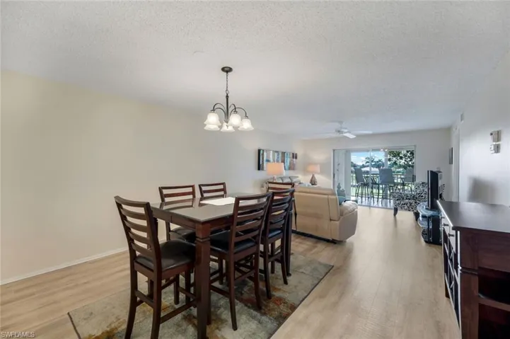Dining space with a textured ceiling, light hardwood / wood-style flooring, and ceiling fan with notable chandelier