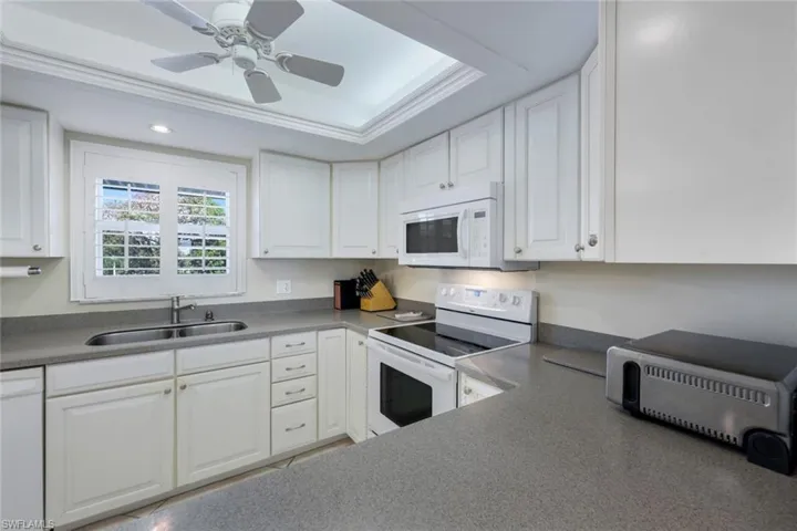 Kitchen featuring white appliances, a tray ceiling, sink, and white cabinets
