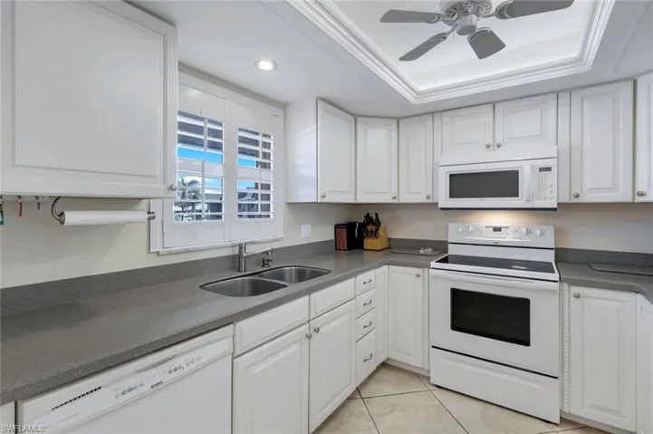 Kitchen with white cabinetry, a tray ceiling, light tile patterned flooring, sink, and white appliances