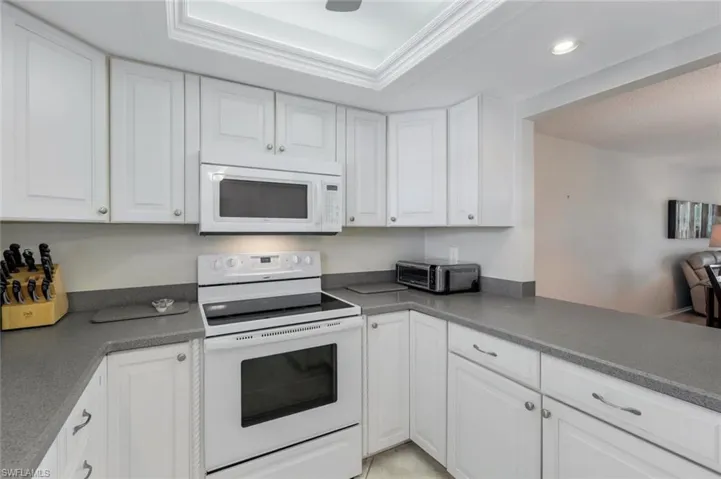Kitchen featuring white cabinets, a tray ceiling, and white appliances