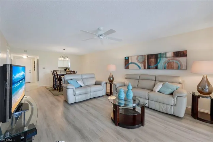 Living room with a textured ceiling, light hardwood / wood-style flooring, and ceiling fan with notable chandelier