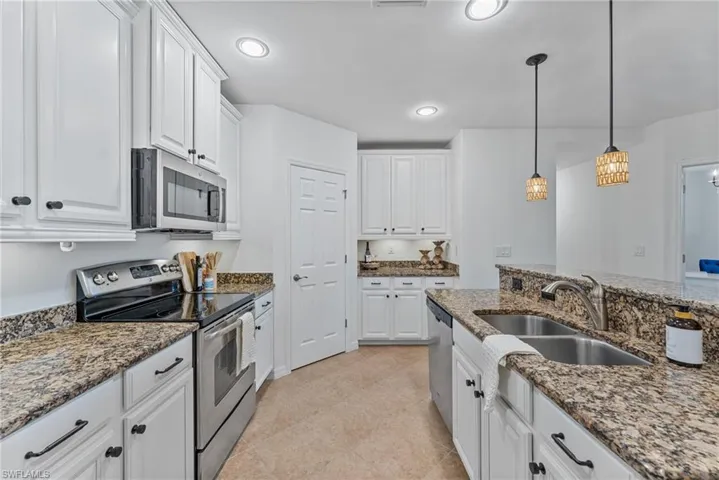 Kitchen with stainless steel appliances, white cabinets, decorative light fixtures, and dark stone countertops