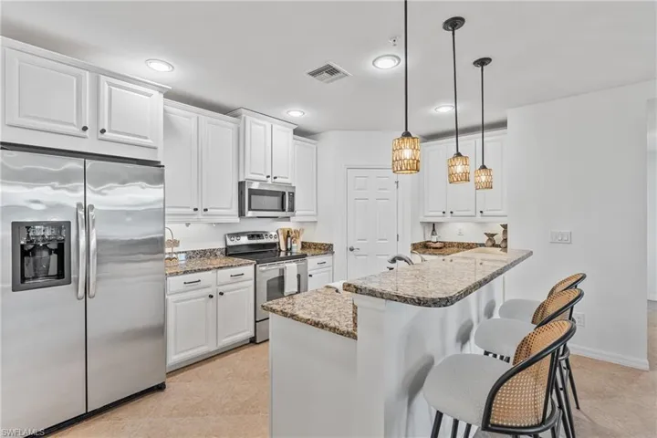 Kitchen with stainless steel appliances, white cabinets, dark stone countertops, pendant lighting, and a breakfast bar