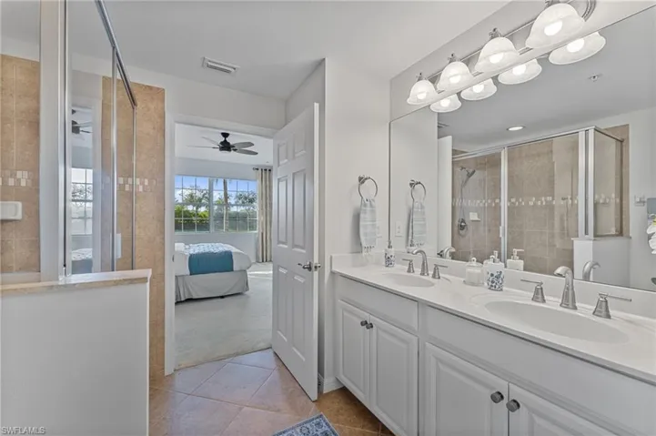 Ensuite bathroom featuring a stall shower, double vanity, light tile patterned flooring, and a ceiling fan