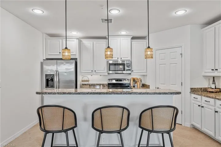 Kitchen with a breakfast bar area, white cabinets, and dark stone counters