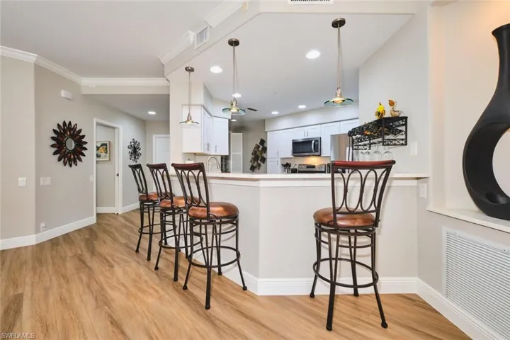 Kitchen with a breakfast bar area, white cabinets, pendant lighting, light wood-style flooring, and stainless steel microwave