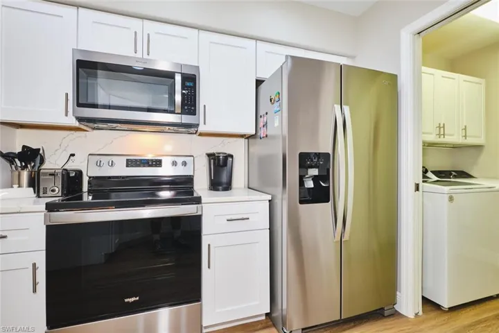 Kitchen with appliances with stainless steel finishes, white cabinetry, backsplash, light wood finished floors, and washer and dryer