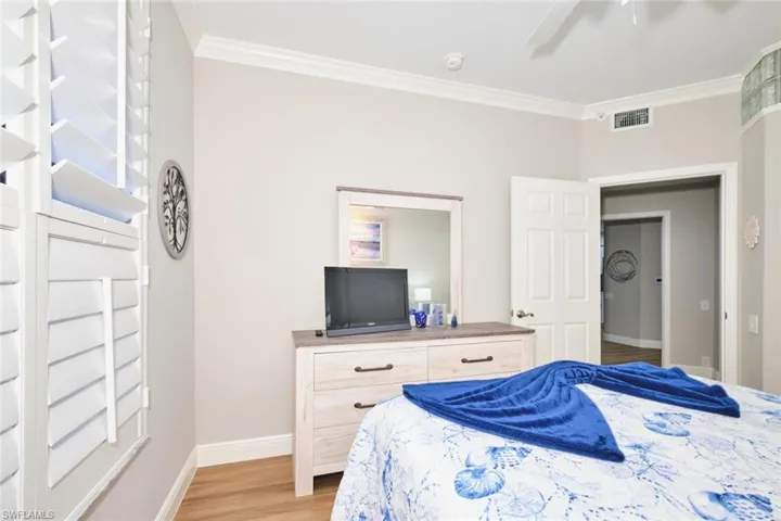Bedroom featuring light wood finished floors, ornamental molding, and a ceiling fan