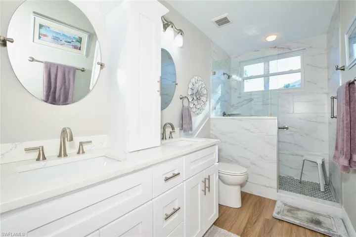 Bathroom featuring double vanity, a marble finish shower, and light wood finished floors