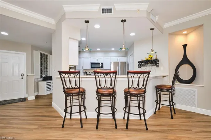 Kitchen with white cabinets, a breakfast bar area, light wood-type flooring, appliances with stainless steel finishes, and decorative light fixtures