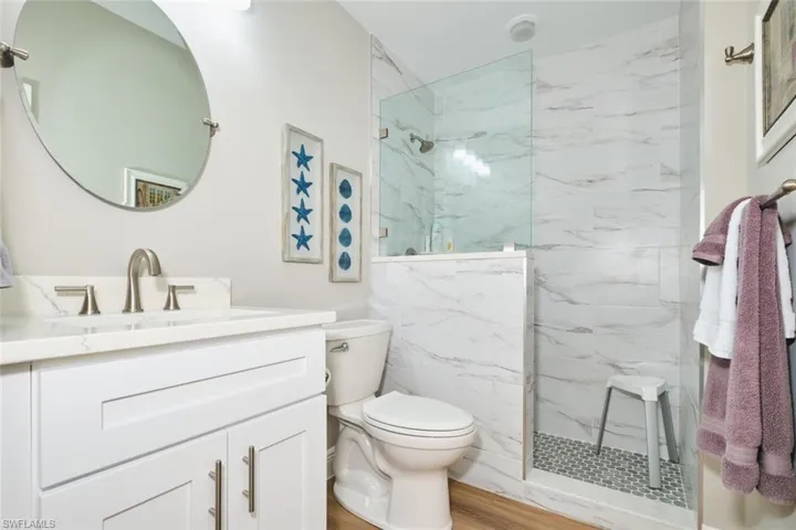 Bathroom with vanity, a marble finish shower, and light wood-style flooring