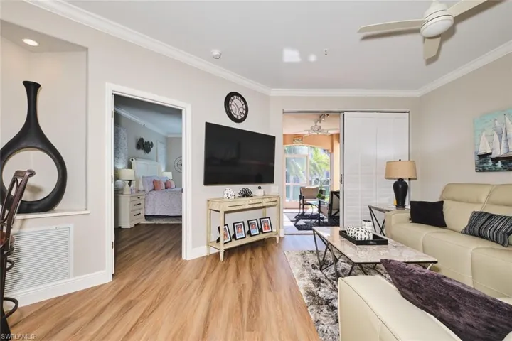 Living room with ceiling fan, ornamental molding, and light wood-type flooring
