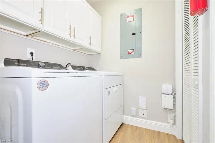 Washroom featuring electric panel, cabinet space, light wood-style floors, and separate washer and dryer