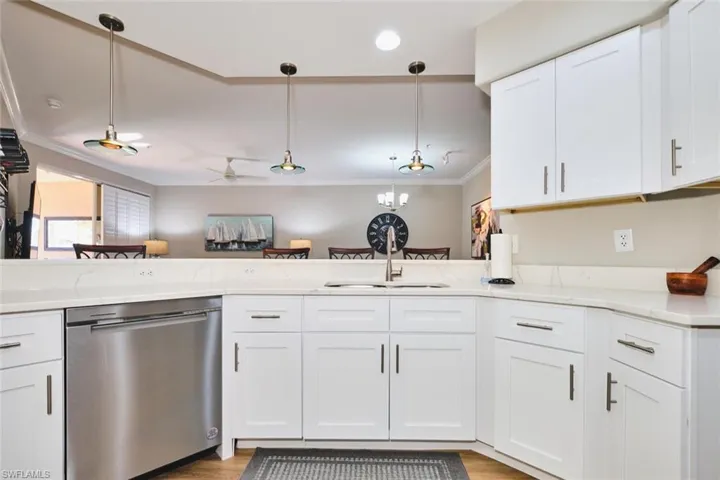 Kitchen with dishwasher, white cabinets, pendant lighting, crown molding, and light wood-type flooring