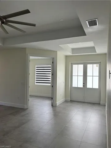 Spare room with a raised ceiling, ceiling fan, french doors, and light tile patterned flooring