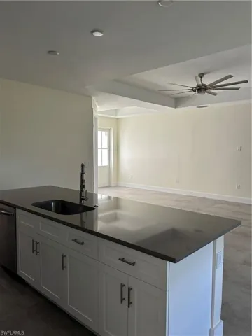 Kitchen with ceiling fan, a kitchen island with sink, dishwashing machine, white cabinets, and open floor plan