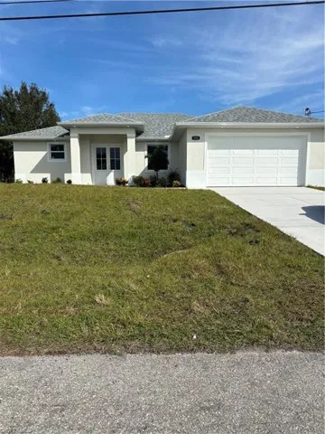 View of front of home with stucco siding, a front lawn, concrete driveway, and a garage