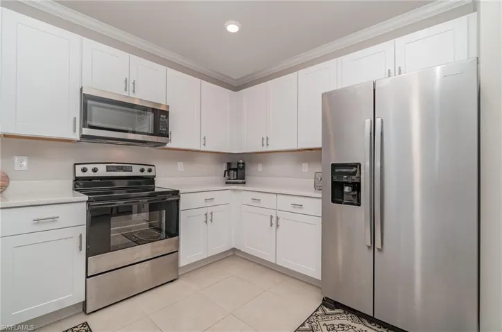 Kitchen featuring crown molding, white cabinets, stainless steel appliances, and light tile patterned floors