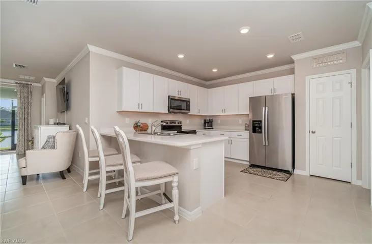 Kitchen featuring a breakfast bar area, ornamental molding, light tile patterned flooring, white cabinetry, and appliances with stainless steel finishes