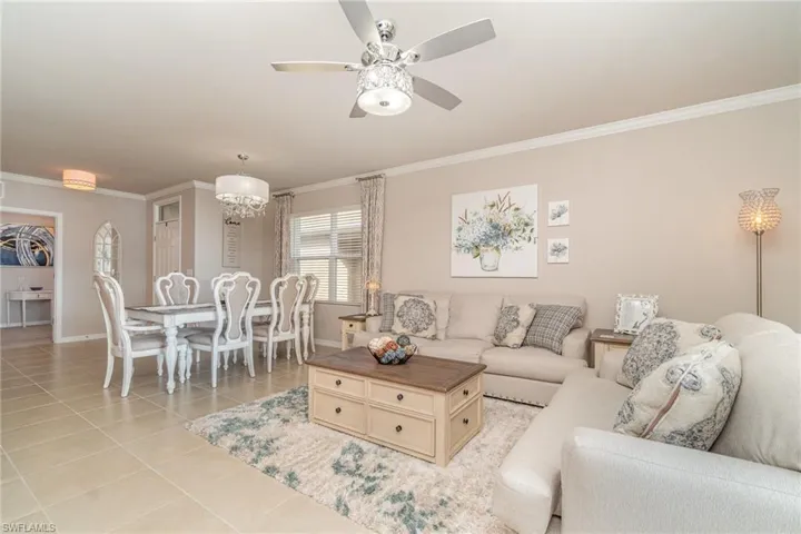 Tiled living room featuring ornamental molding and ceiling fan with notable chandelier