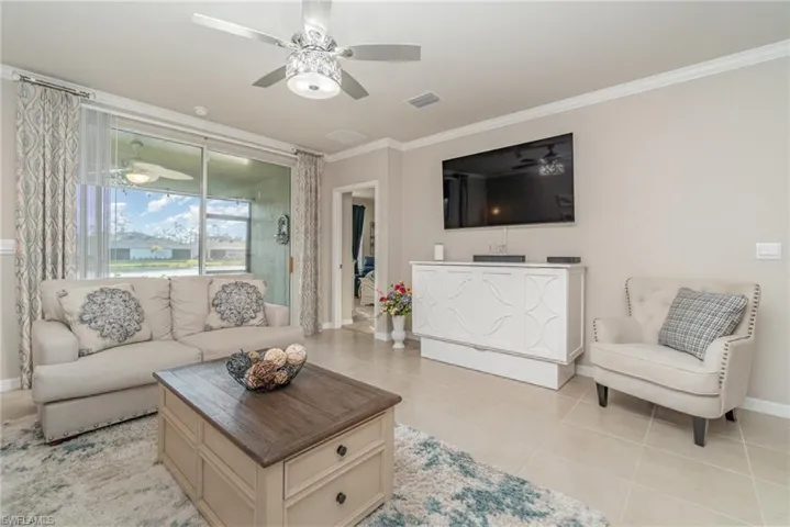 Living room featuring ceiling fan, ornamental molding, and light tile patterned flooring