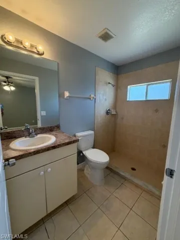 Full bathroom featuring a tile shower, vanity, light tile patterned floors, and a textured ceiling