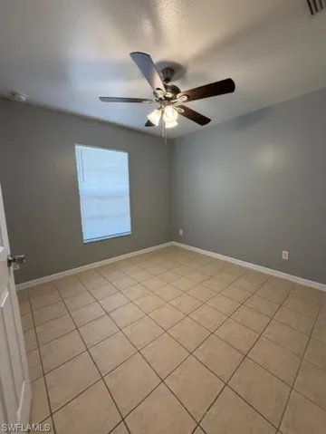 Empty room with ceiling fan, a textured ceiling, and light tile patterned flooring