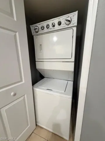 Laundry area featuring light tile patterned floors and stacked washing machine and dryer