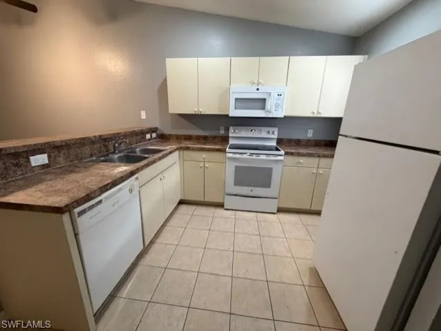 Kitchen with dark countertops, white appliances, light tile patterned floors, a peninsula, and vaulted ceiling