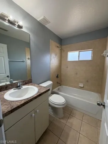 Bathroom featuring vanity, washtub / shower combination, light tile patterned floors, a textured ceiling, and a textured wall