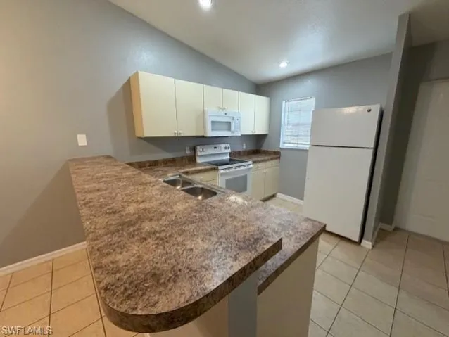Kitchen with white appliances, a peninsula, dark countertops, light tile patterned floors, and lofted ceiling