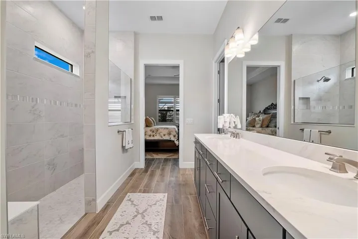Bathroom with wood-type flooring, tiled shower, double sink, and vanity with extensive cabinet space