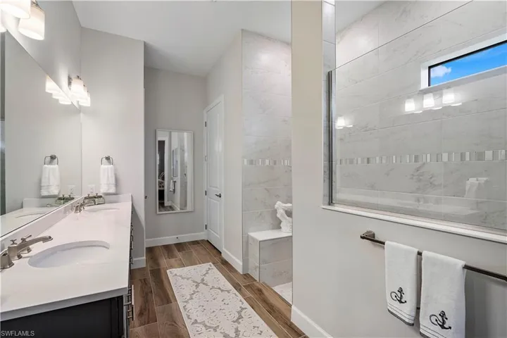 Bathroom with a tile shower, dual sinks, vanity with extensive cabinet space, and wood-type flooring