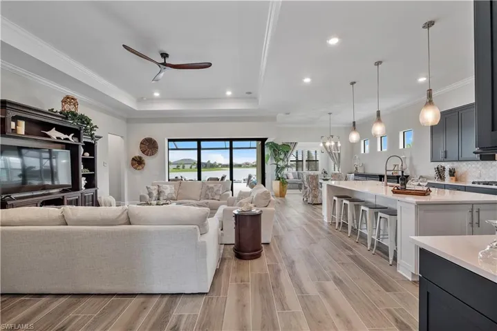 Living room with ceiling fan with notable chandelier, a tray ceiling, light hardwood / wood-style floors, and ornamental molding