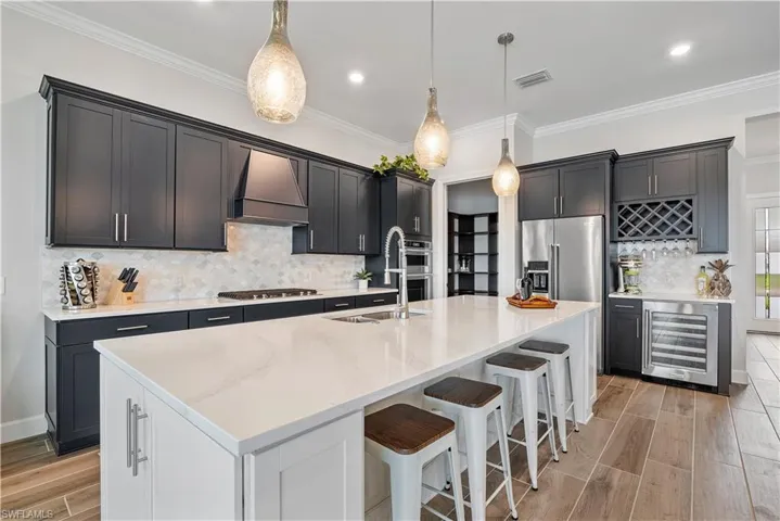Kitchen with premium range hood, a kitchen island with sink, beverage cooler, backsplash, and pendant lighting