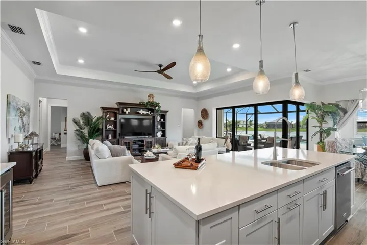 Kitchen featuring hanging light fixtures, a raised ceiling, and a kitchen island with sink