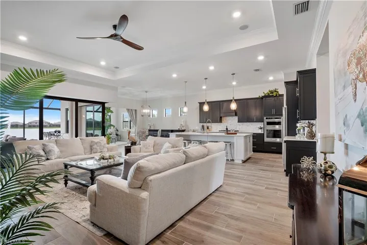 Living room featuring ceiling fan, ornamental molding, a tray ceiling, and light hardwood / wood-style floors