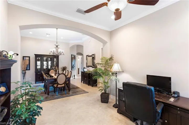 Home office with light tile patterned flooring, ceiling fan with notable chandelier, and crown molding