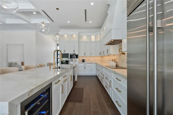 Kitchen featuring custom exhaust hood, white cabinetry, appliances with stainless steel finishes, beverage cooler, and light stone countertops