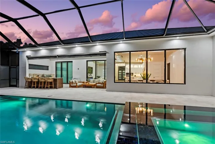 Pool at dusk with a bar, an outdoor living space, a lanai, and a patio area