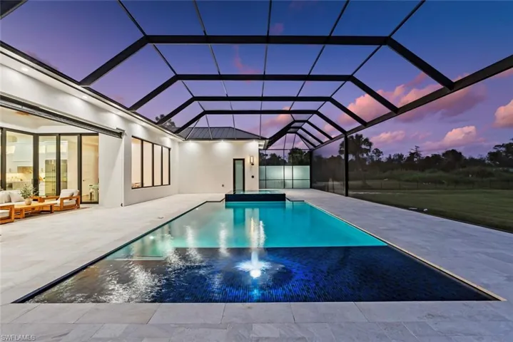 Pool at dusk featuring an outdoor living space, a patio area, and glass enclosure