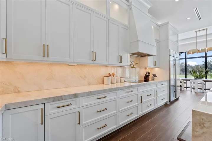 Kitchen featuring white cabinetry, black electric stovetop, light stone countertops, custom range hood, and decorative backsplash